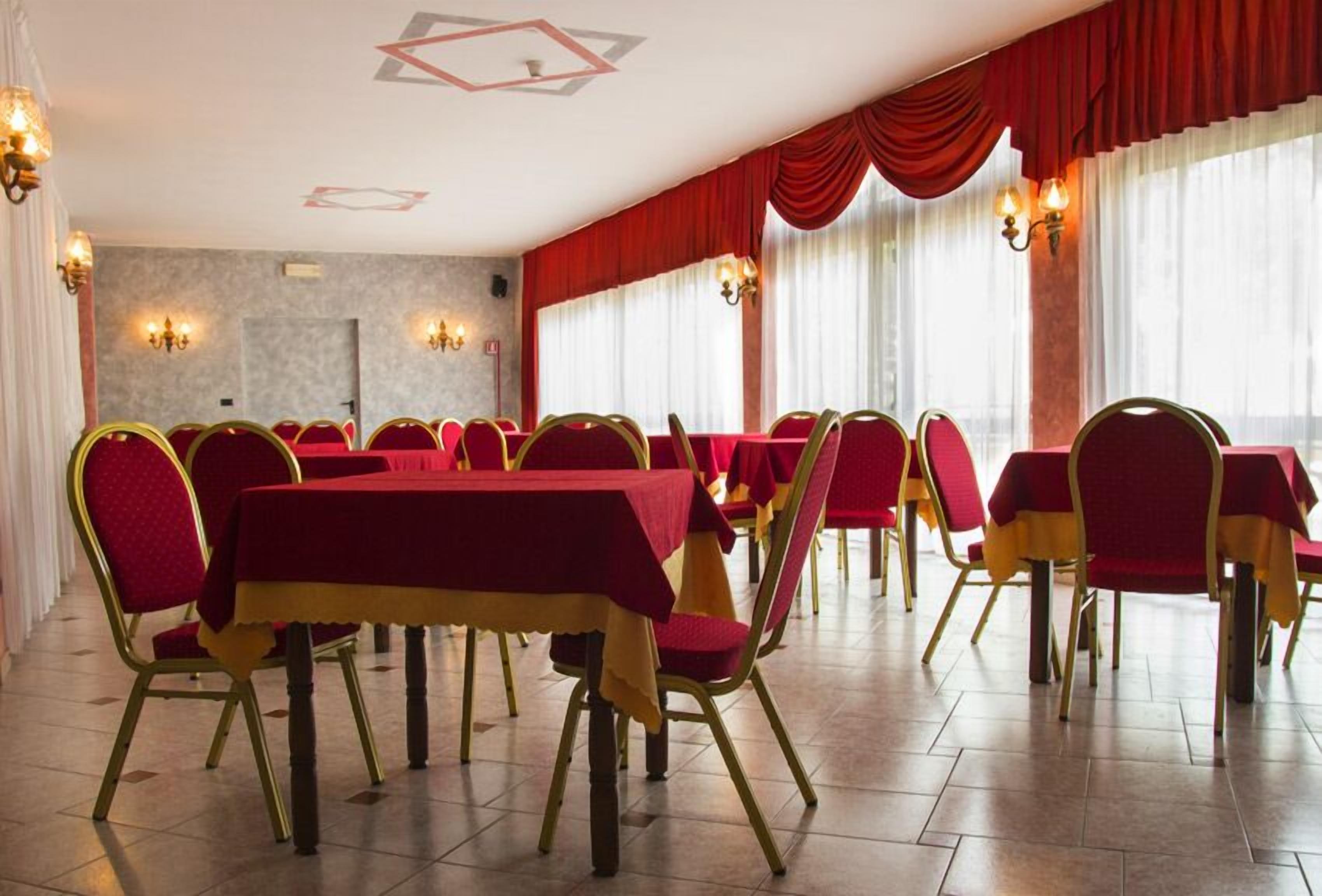A banquet hall with red tables and chairs, chandeliers, and large windows with red curtains.
