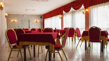 A banquet hall with red tables and chairs, chandeliers, and large windows with red curtains.