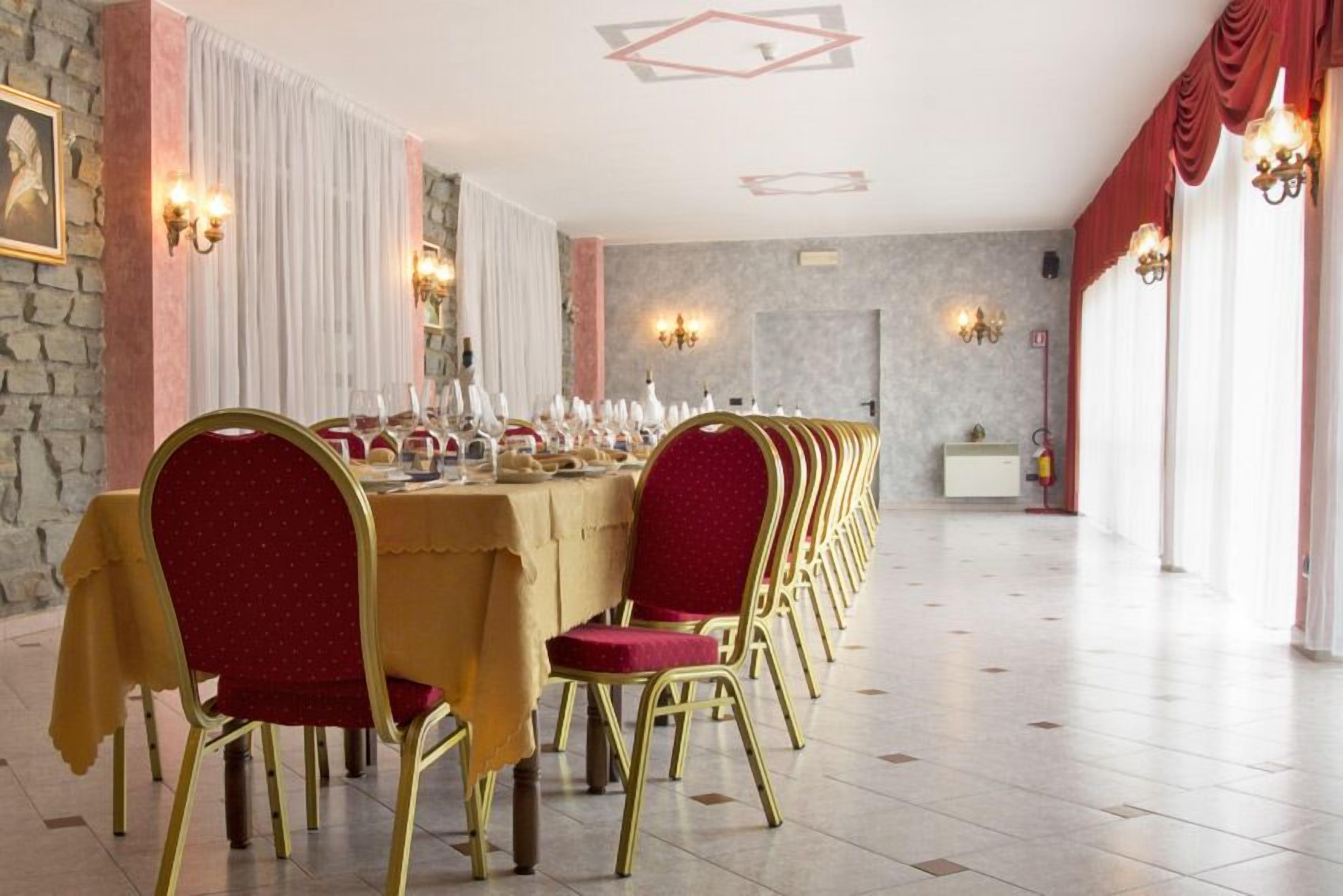 Ein langer Esstisch mit rot gepolsterten Stühlen und goldenen Rahmen, gedeckt für ein festliches Mahl in einem geräumigen Raum mit Steinwänden und dekorativer Beleuchtung.