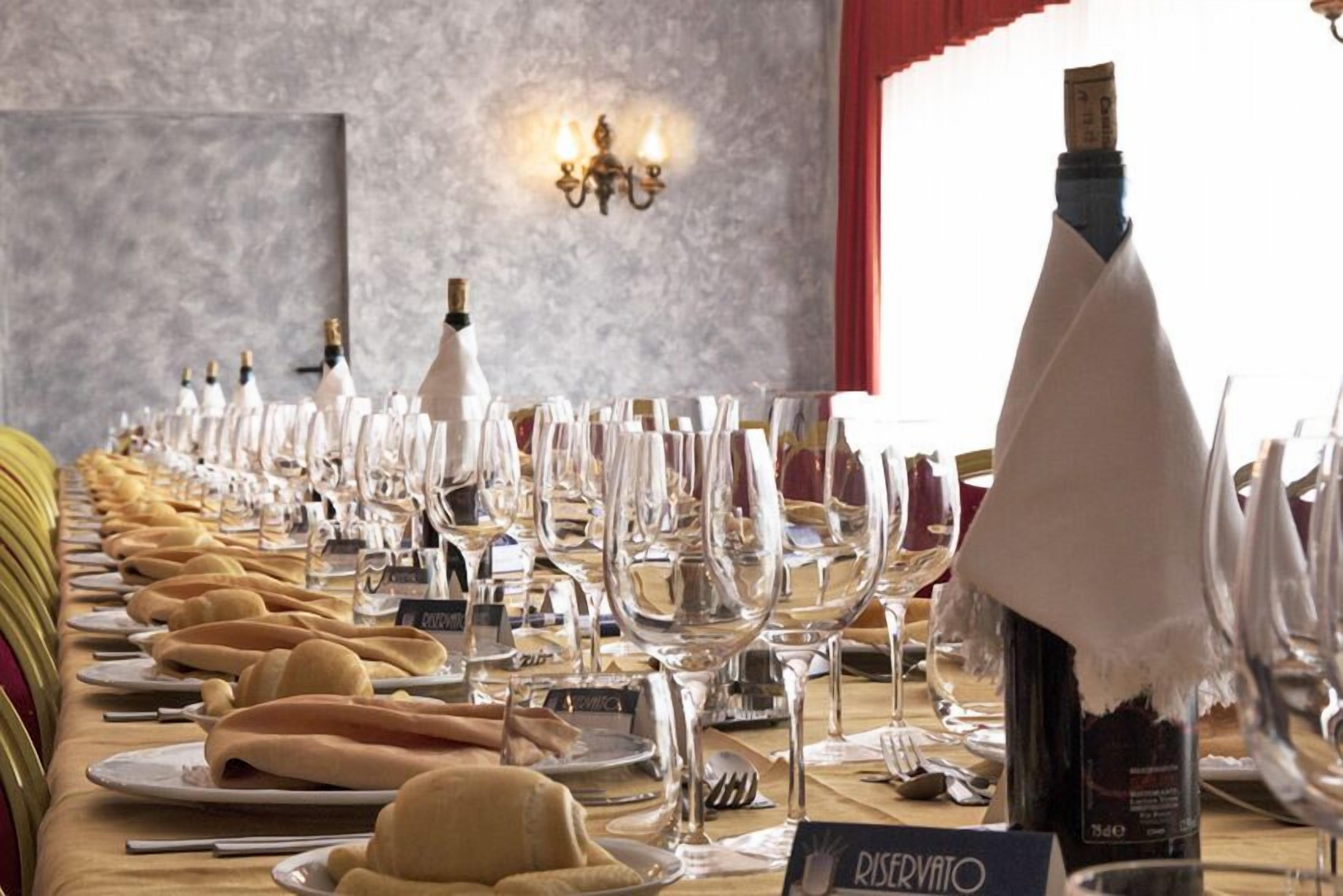 A long table set for a formal dining event with wine glasses, plates, and a bottle of wine.