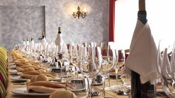 A long table set for a formal dining event with wine glasses, plates, and a bottle of wine.