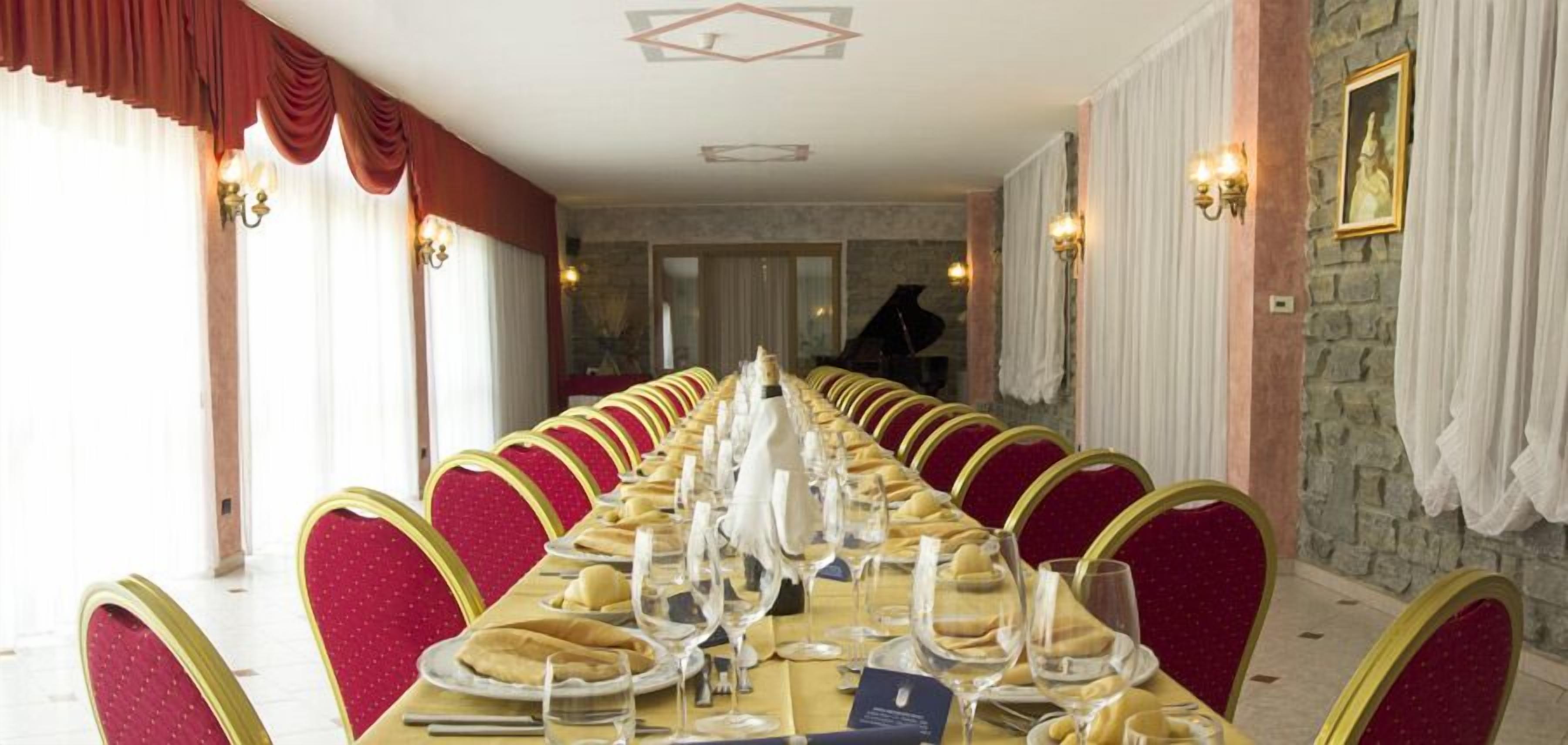 A long dining table set for a formal meal with red upholstered chairs and gold accents.