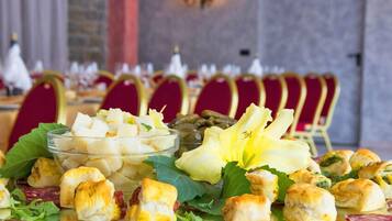 Ein Tisch mit verschiedenen Vorspeisen, darunter gewürfelter Käse, gefüllte Teigtaschen und Blattsalat, vor einer Kulisse aus roten Stühlen und einer Steinsäule.