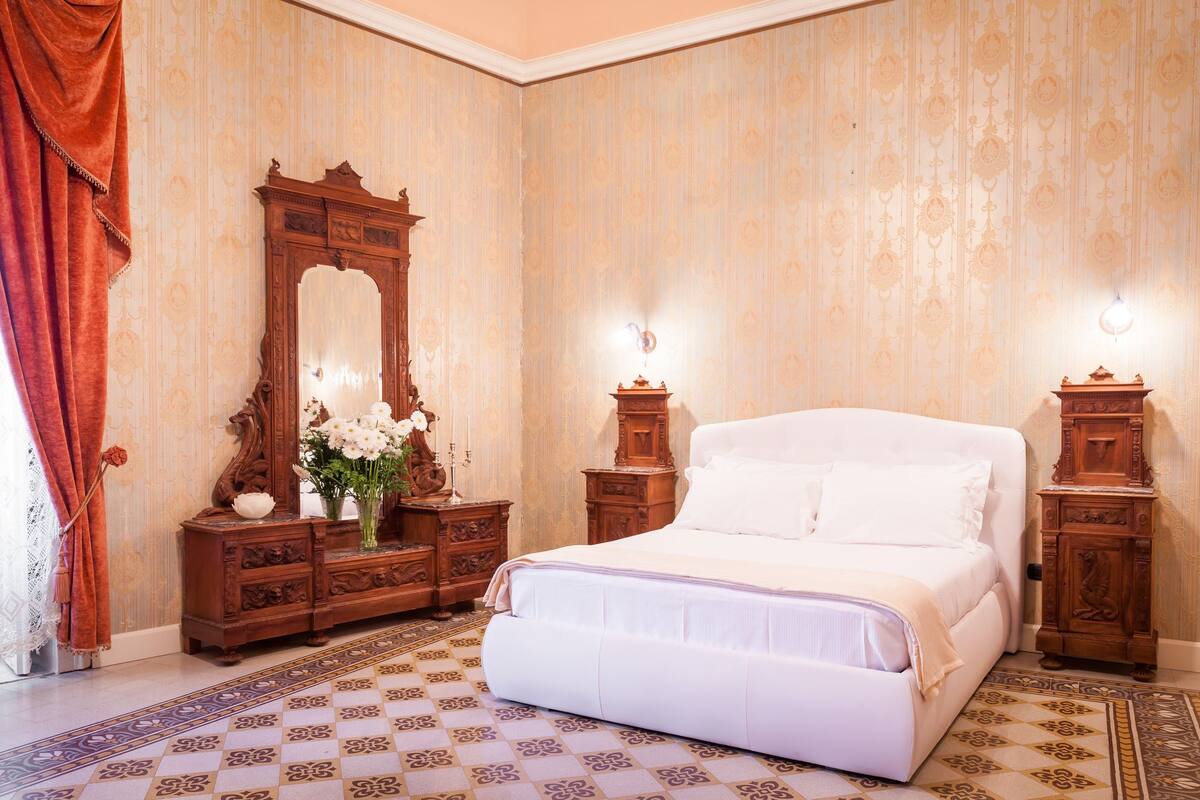 A bedroom with a large bed, wooden dresser, and a mirror.