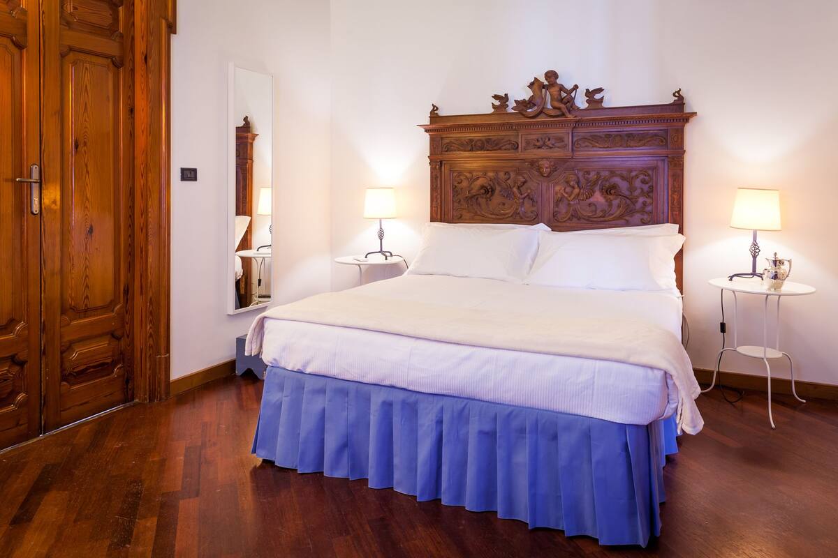 A neatly made bed with a wooden headboard, two bedside tables with lamps, and a wooden wardrobe.