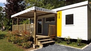 Een stacaravan met een overdekte veranda, een klein terras en een geel accentmuur.