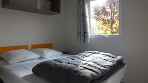 Een eenpersoonsbed met een grijze dekbedovertrek en witte kussens in een kamer met een raam en een wandplank.