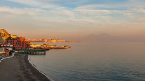 A coastal scene with a beach, buildings, and a pier extending into calm waters. - O House Posillipo by Napoliapartments (Naples)