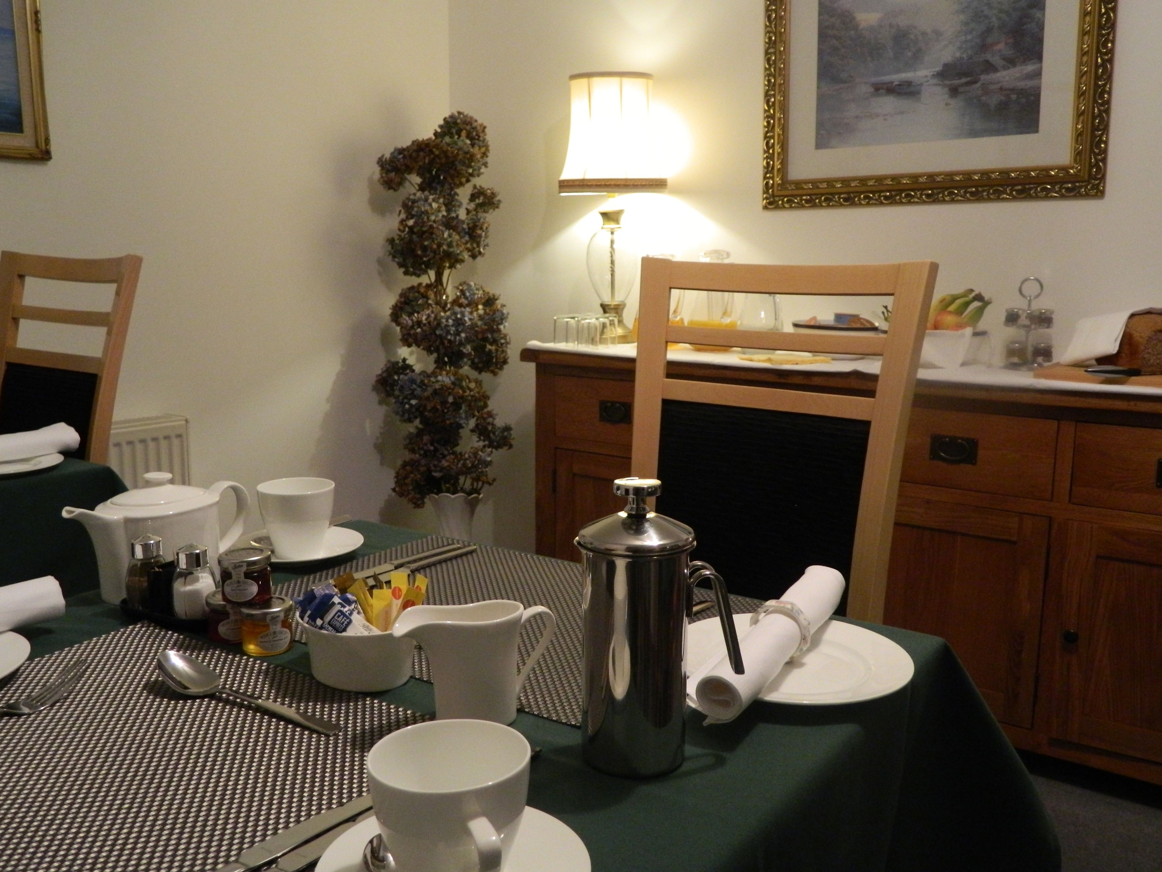 Un comedor con una mesa preparada para dos personas, incluyendo una jarrón, tazas y una tetera.