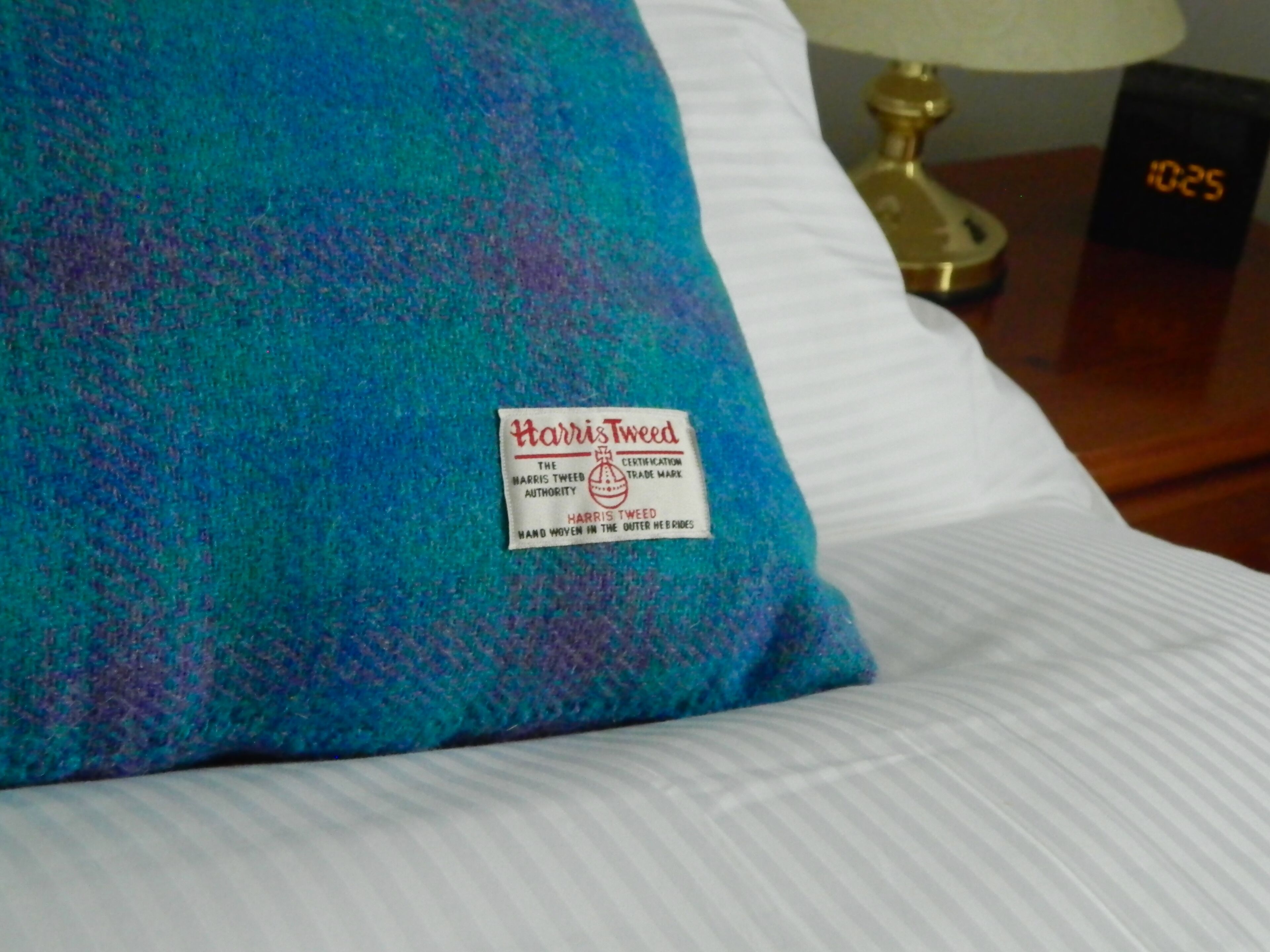 Un coussin en tweed Harris sur un lit, avec une taie d’oreiller blanche.