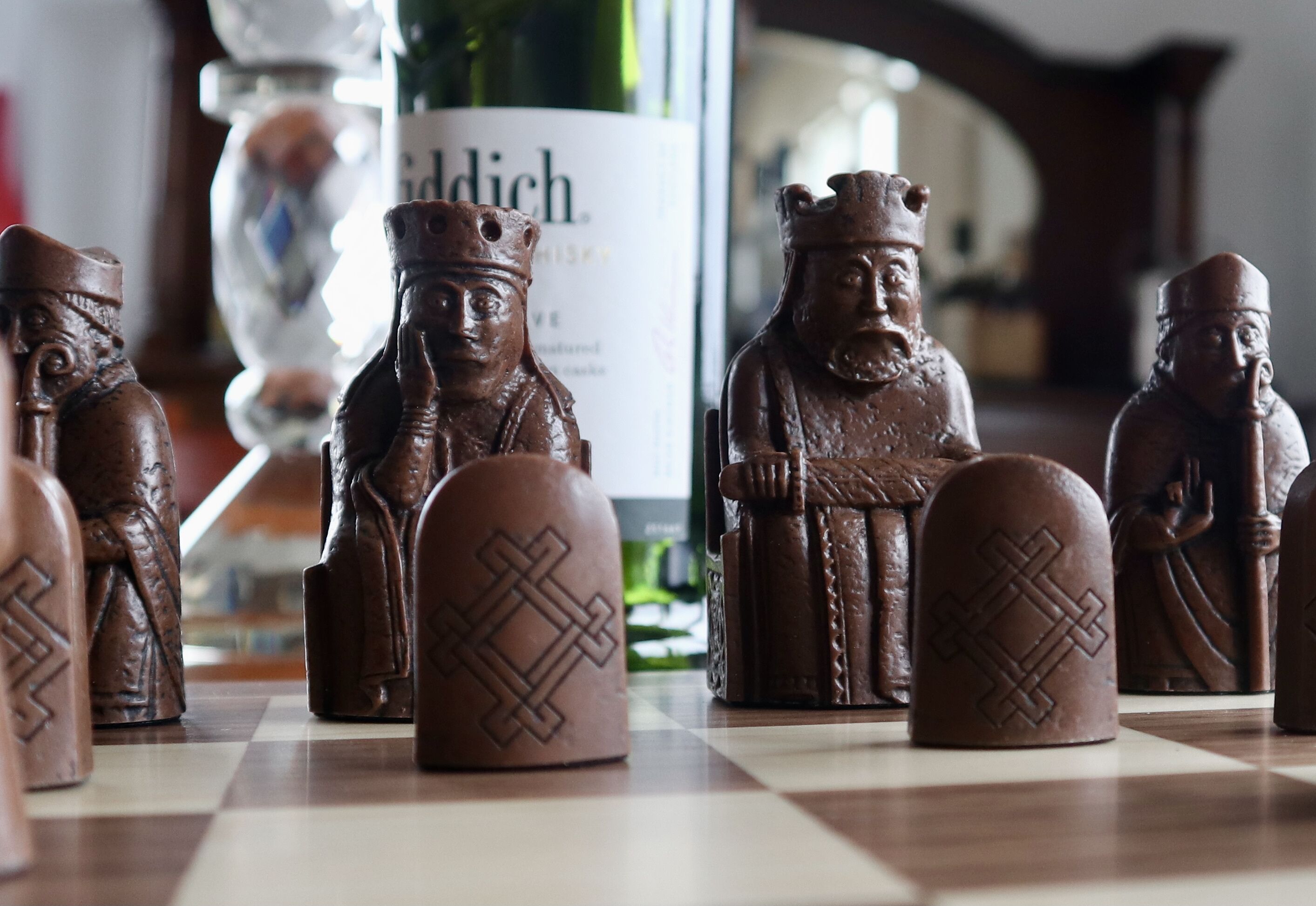 A chessboard with wooden figurines and a bottle labeled "Siddich" in the background.