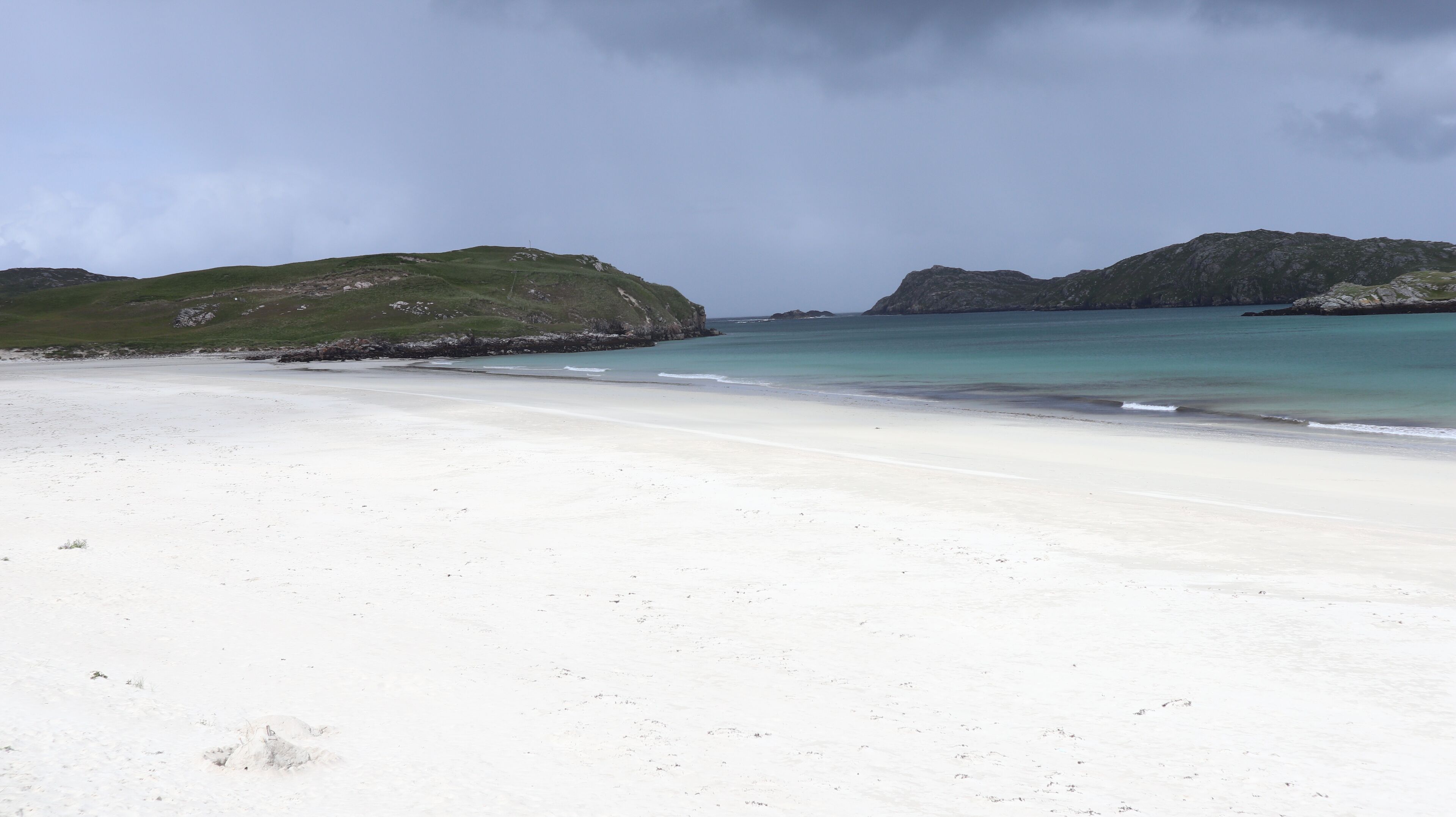 Ein Strand mit weißem Sand und ruhigem türkisblauem Wasser, umgeben von grünen Hügeln.