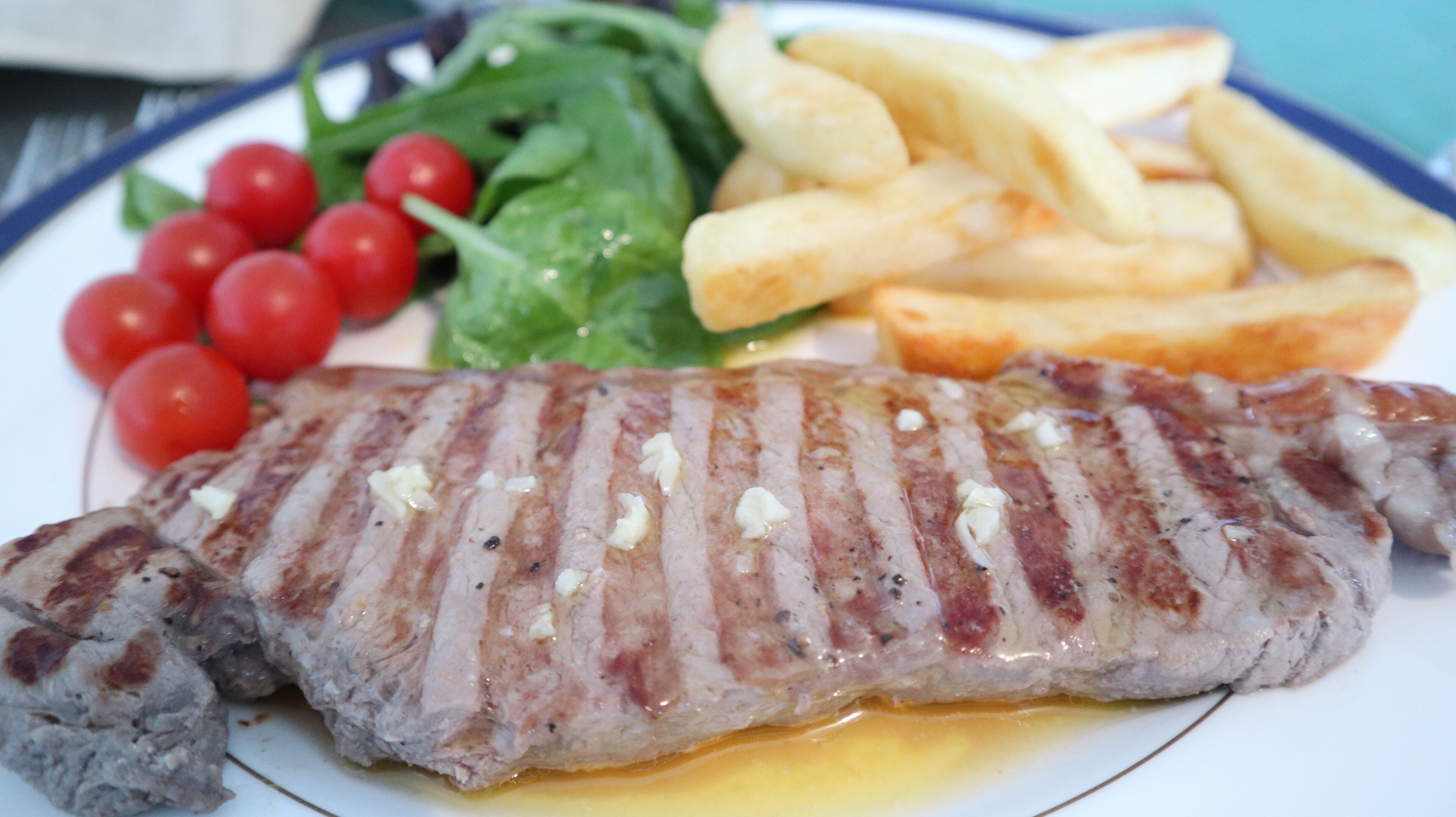 A plate with grilled steak, French fries, cherry tomatoes, and a green salad.