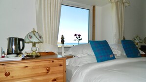 Et hotelværelse med seng, et træskab, en lampe og havudsigt fra vinduet.
