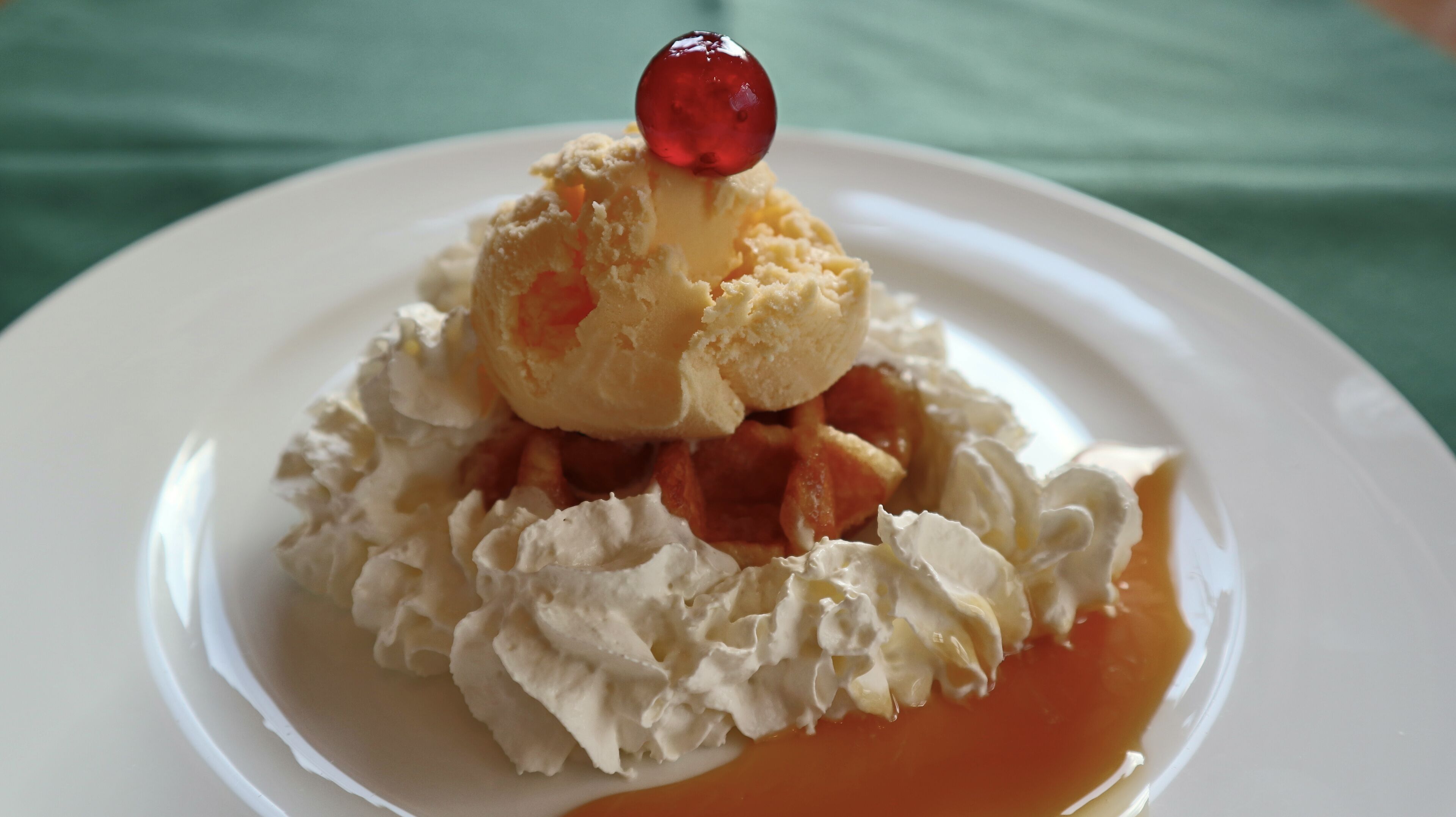 A dessert with ice cream, whipped cream, and a cherry on top, served on a white plate.