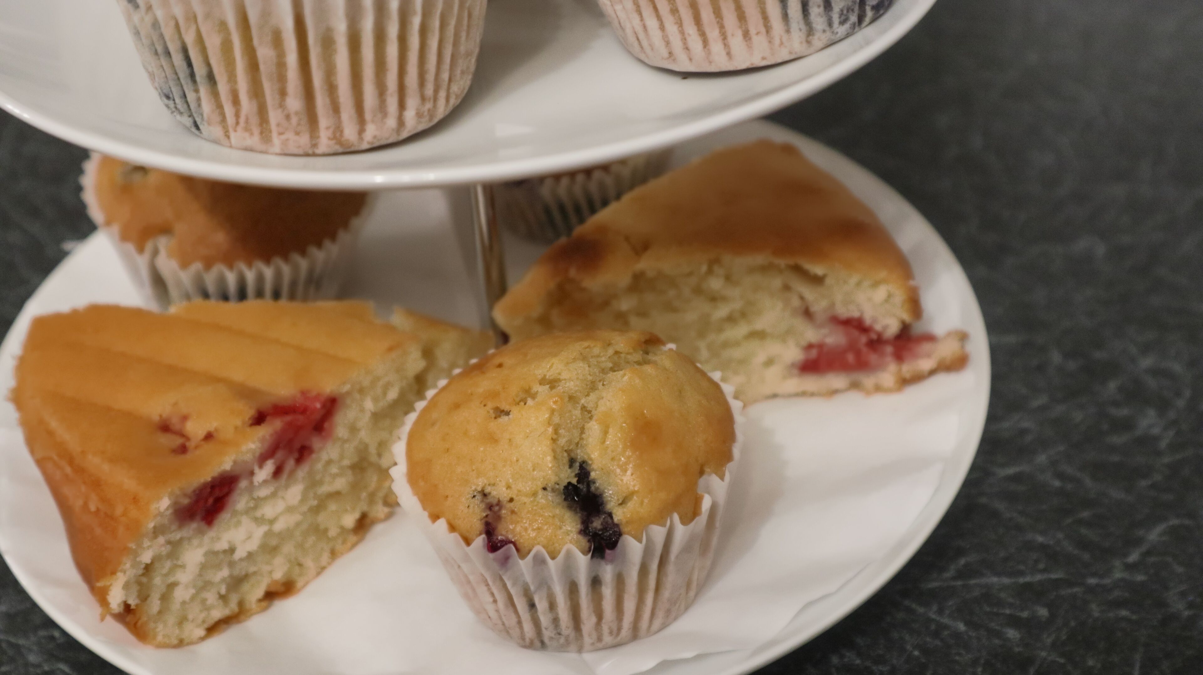 En tallerken med tre muffins, hvoraf den ene er skåret over og viser en rød frugtfyld.