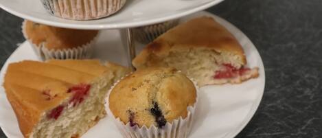 En tallerken med tre muffins, hvoraf den ene er skåret over og viser en rød frugtfyld.