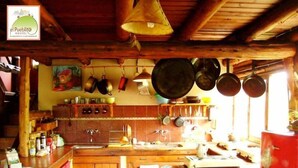 A rustic kitchen with wooden beams, hanging pots, and a brick backsplash. - El Pueblito Ecohostel (El Bolson)