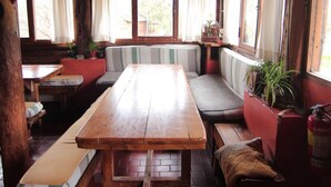 A rustic wooden interior with a long table, benches, and a red cushioned bench. - El Pueblito Ecohostel (El Bolson)