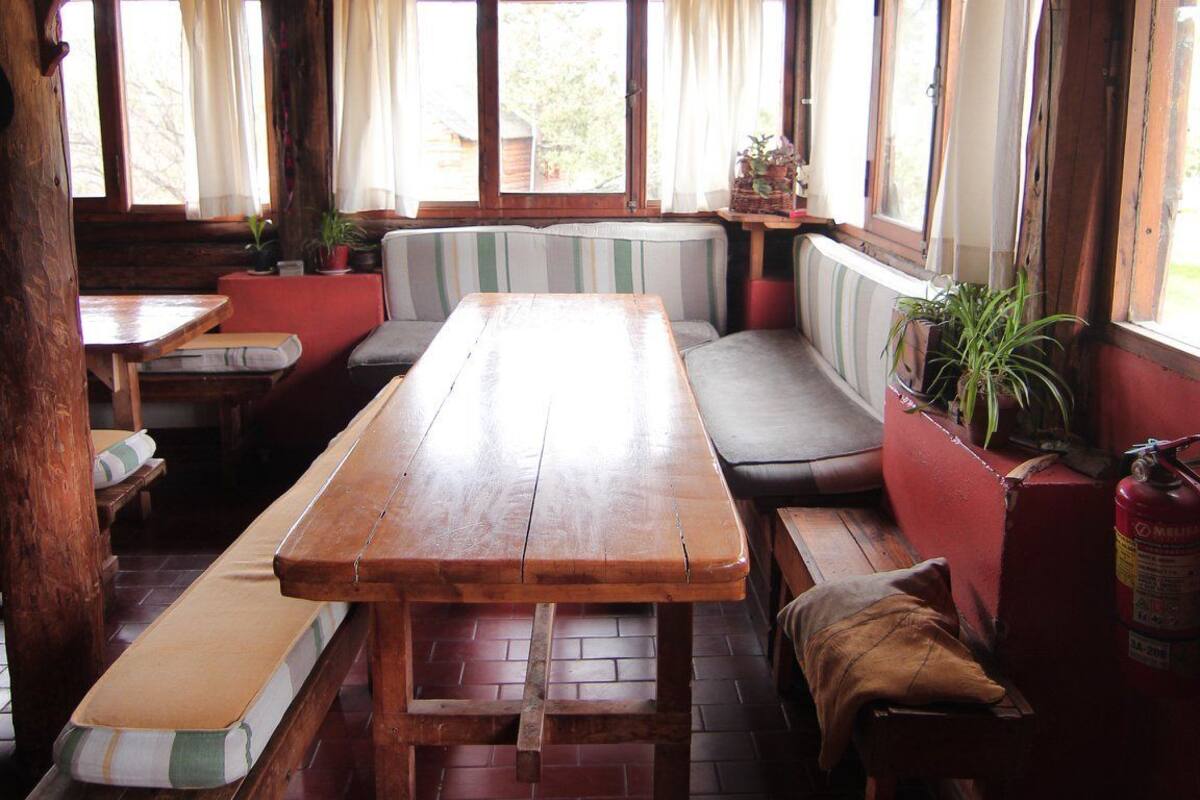 A rustic wooden interior with a long table, benches, and a red cushioned bench.