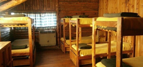 Una cabaña con cuatro literas dispuestas en fila, paredes de madera y una ventana con cortina escocesa.