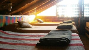 A cozy attic room with three beds, a wooden ceiling, and a view of the outside. - El Pueblito Ecohostel (El Bolson)