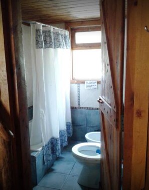A narrow bathroom with two toilets, a shower curtain, and a window. - El Pueblito Ecohostel (El Bolson)