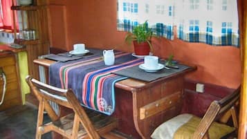 Un pequeño comedor con una mesa de madera, dos sillas, un mantel a rayas y una planta en maceta.