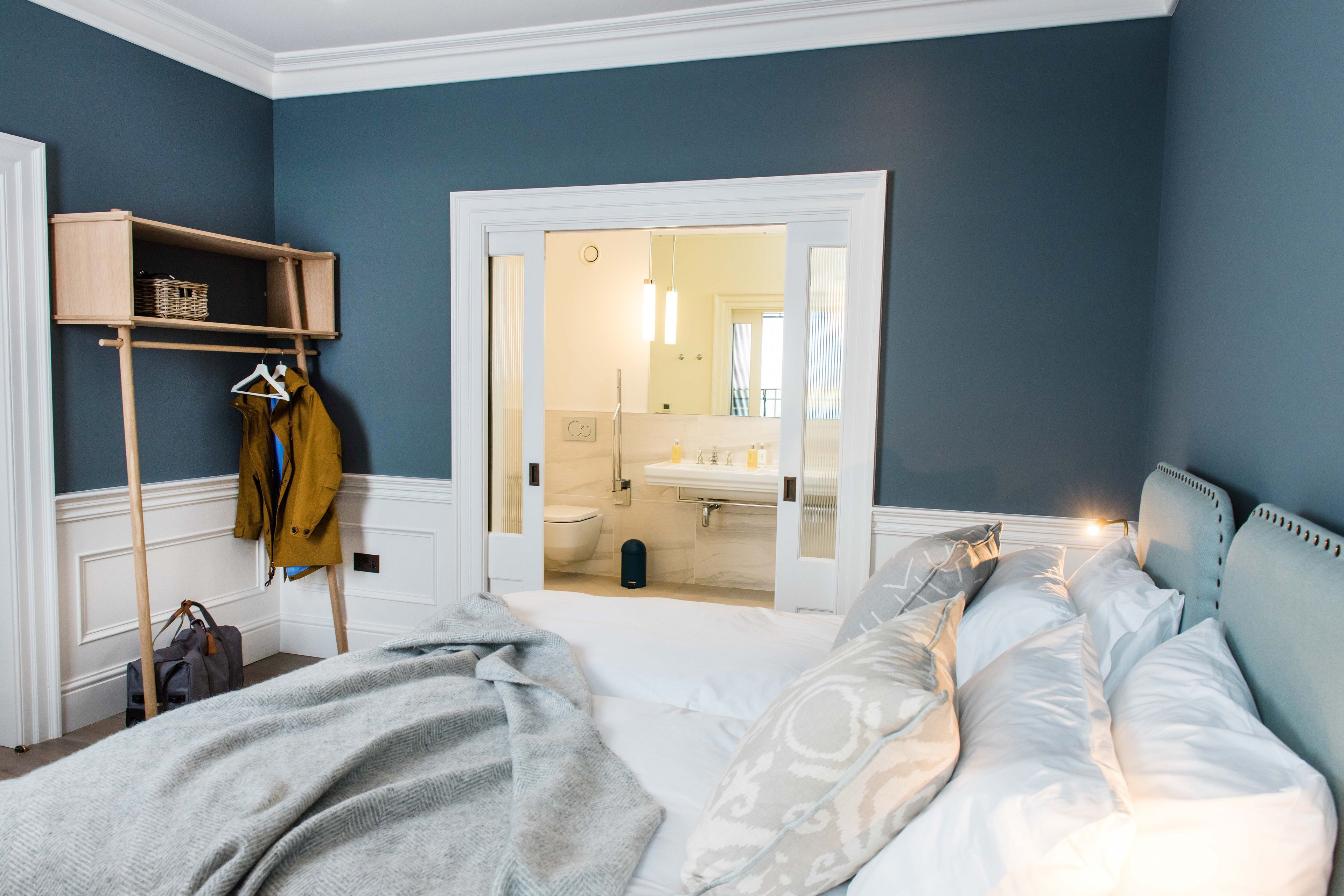 A bedroom with a bed, a wooden wardrobe, and a bathroom visible through an open door.