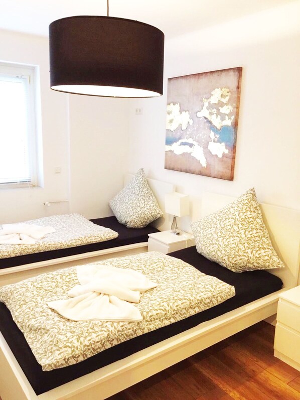 A modern bedroom with two beds, a large hanging lamp, and a wall-mounted abstract painting. - City Apartment Hannover (Hannover)
