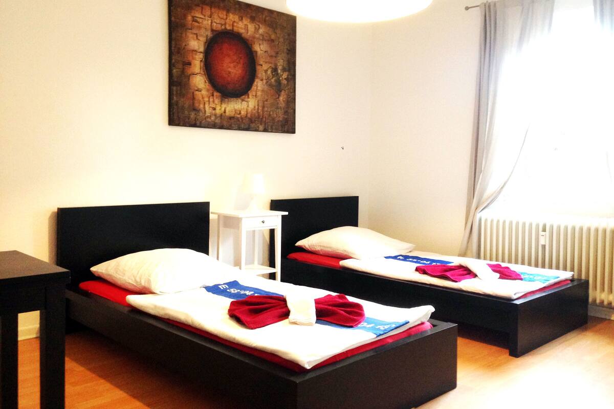 Habitación de hotel con dos camas, un cuadro en la pared, una lámpara y una ventana con cortinas.