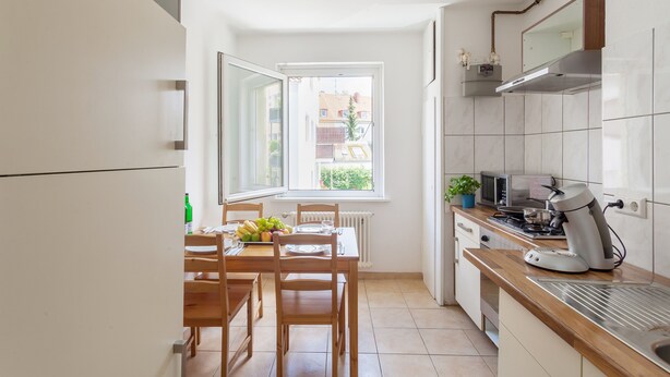 A compact kitchen with a dining table, chairs, a stove, and a window providing a view of buildings outside. - City Apartment Hannover (Hannover)