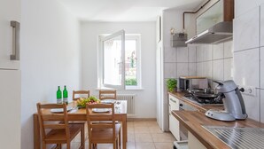 A modern kitchen with a dining area, featuring a wooden table, chairs, a coffee machine, and a view through a window. - City Apartment Hannover (Hannover)