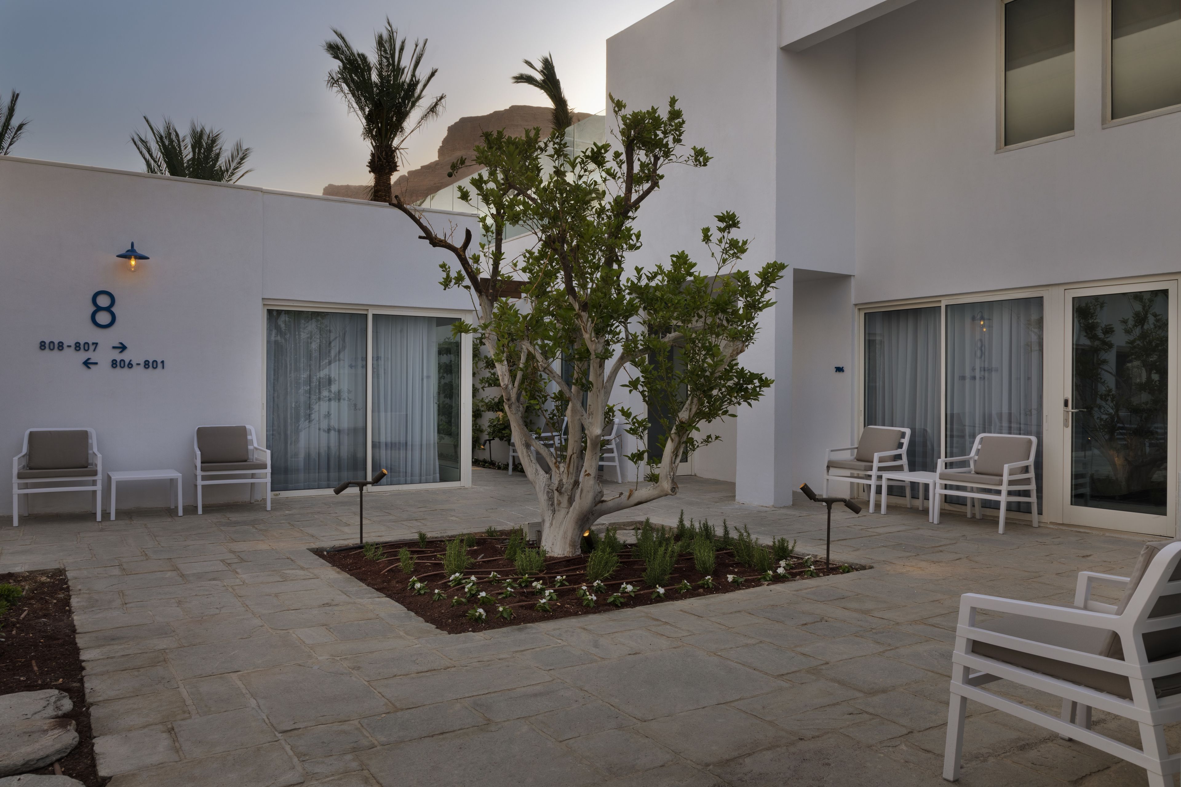A modern building with a number '8' sign, outdoor seating, and a tree in the courtyard.