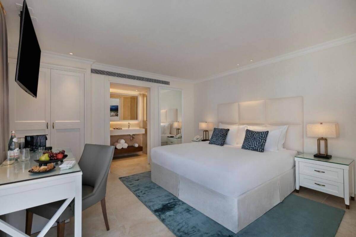 A hotel room with a large bed, bedside tables, a desk with a chair, a TV, and a bathroom with a mirror.