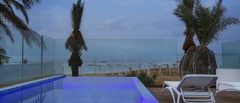 Un área de piscina con agua azul cristalina, rodeada de palmeras y sillones blancos.