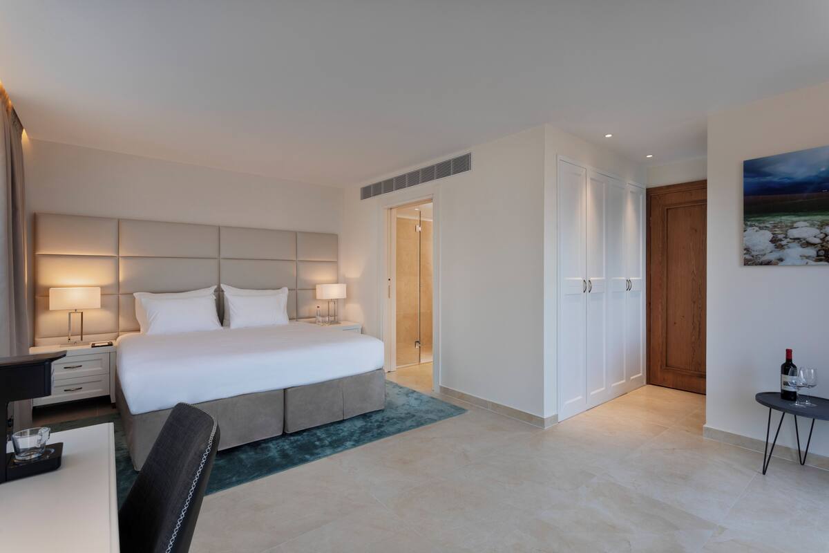 A modern hotel room with a large bed, bedside tables, a desk, and a chair.