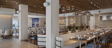 A modern dining area with long tables, cushioned seating, and pendant lighting.