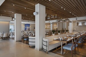Un comedor moderno con mesas largas, asientos acolchados e iluminación colgante.