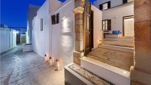 Een luxe villa met een gevel van natuursteen, een bordje met de tekst 'Indos Allure Luxury Villa' en een goed verlicht interieur met een bank en een kamerbreed tapijt.
