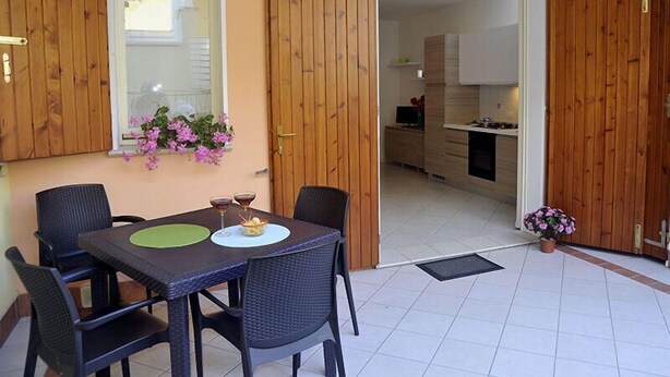 Un coin repas avec une table et des chaises, une fenêtre ornée de fleurs et des portes en bois donnant sur une cuisine.