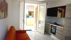 Un espace de vie compact comprenant un canapé, un coin cuisine et une porte ouverte donnant sur un balcon.