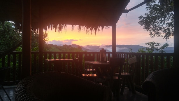 A wooden deck with tables and chairs, overlooking a mountainous landscape during sunset. - Finca De Buen Consejo - Hostel (Pacto)