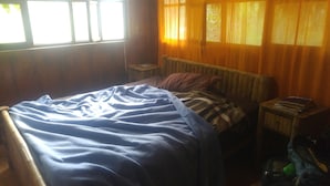 A room with a bed, a nightstand, a radiator, and a window with curtains. - Finca De Buen Consejo - Hostel (Pacto)