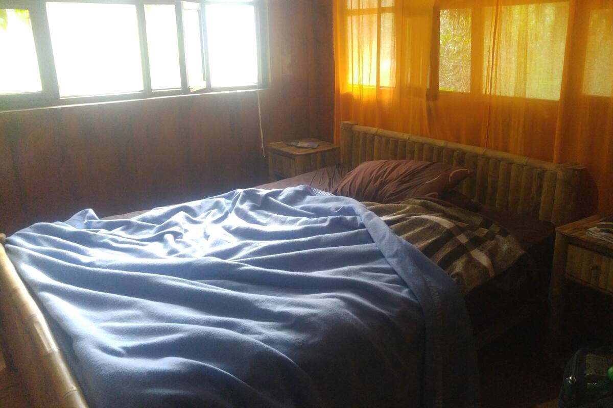 Una habitación con cama, mesita de noche, radiador y ventana con cortinas.