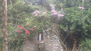 A stone structure with a statue, surrounded by lush greenery and flowering plants. - Finca De Buen Consejo - Hostel (Pacto)