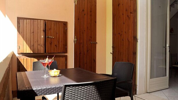 Un patio con mesa y sillas, puertas de madera y un ventanal de vidrio que da a un espacio interior.