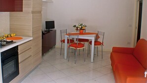 Cocina compacta con comedor, televisor y sofá rojo.