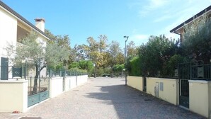Un sendero pavimentado con una puerta, rodeado de edificios y árboles.
