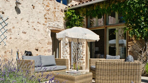 A stone building with a rustic exterior, a wicker sofa set with cushions, and a large umbrella. - Les Picardies (Lesterps)